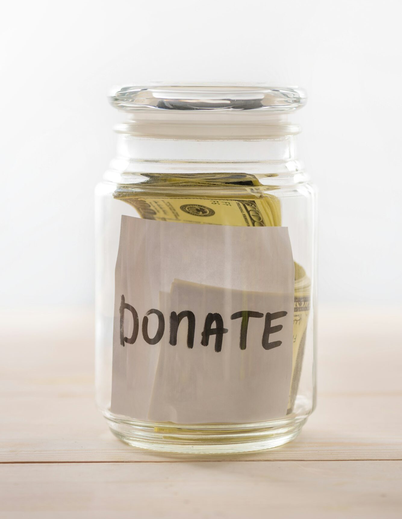 Close-up view of dollar banknotes in glass jar with donate lettering isolated on white, donation